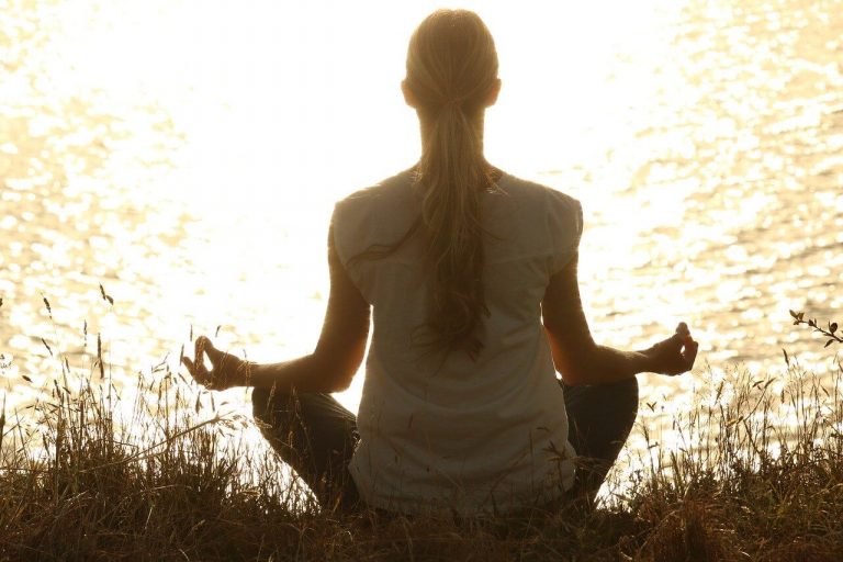 woman mediating on the grassy shore of a lake: self awareness