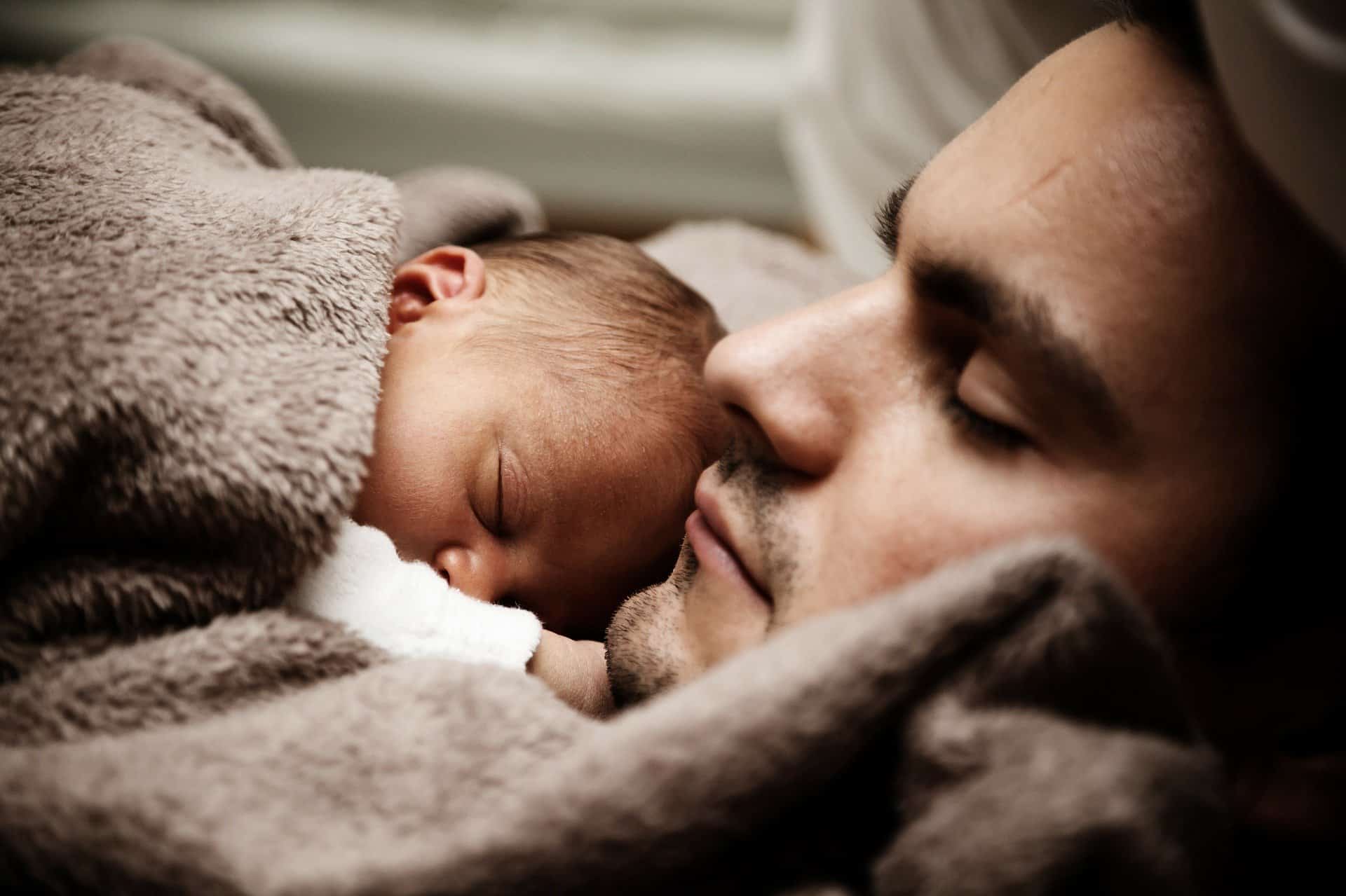 dad sleeping with newborn child fuzzy earth colored blanket